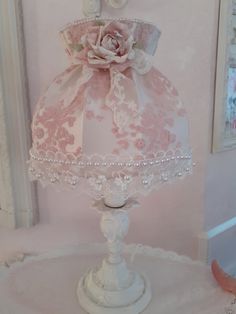 a pink lamp shade with white lace and flowers on the top is sitting on a table