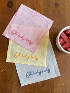 three napkins with embroidered words on them next to a bowl of crayons