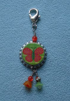 a bottle cap charm with a butterfly on it's side and beads hanging from the bottom