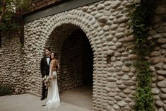 a bride and groom standing in front of an old stone tunnel at the end of their wedding day