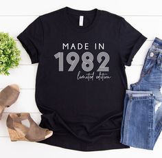 a t - shirt that reads made in 1932 and is next to some jeans, shoes and flowers