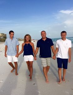 three men and two women walking on the beach with their hands in each other's pockets