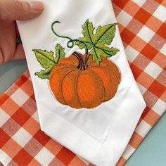 a hand is holding an orange and white napkin with a pumpkin embroidered on the front