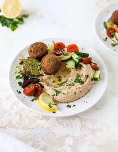 two white plates filled with hummus, tomatoes, cucumbers and lettuce