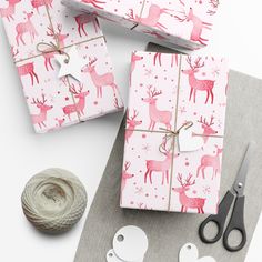 wrapping presents with pink deer and snowflakes on them next to twine of scissors