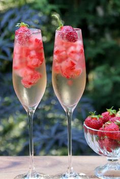 two champagne flutes with strawberries in them sitting on a table next to a bowl of berries