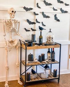 a skeleton is standing next to a shelf with liquor bottles and candles on it in front of a wall decorated with bats