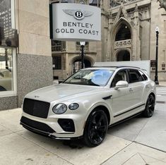 a white bentley suv parked in front of a building