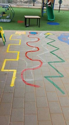 a child's play area with chalk writing on the ground and playground equipment in the background