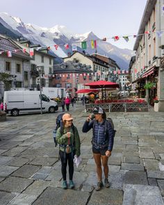 two women are walking down the street in front of some buildings with mountains in the background