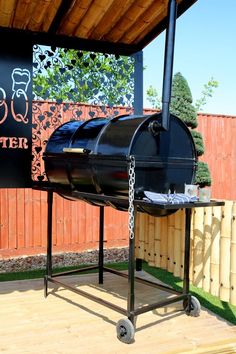 an outdoor bbq grill on wheels in front of a wooden fence with a sign