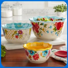 three flowered bowls are sitting on a kitchen counter with utensils in the background