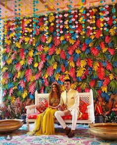 a man and woman sitting on a bench in front of a wall with paper flowers