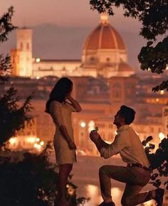 a man kneeling down next to a woman in front of a cityscape at night