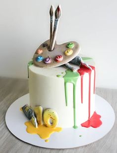 a cake decorated with paint and brushes on top of a white plate that is sitting on a wooden table