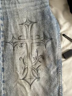 a jean jacket with a cross drawn on it next to a cell phone and pen