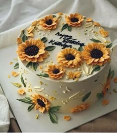 a birthday cake decorated with sunflowers on top of a white sheet covered table