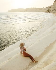 a woman sitting on top of a sandy beach next to the ocean