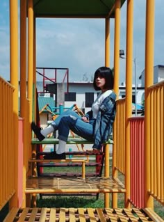 a woman sitting on top of a wooden bench next to a yellow structure and green grass