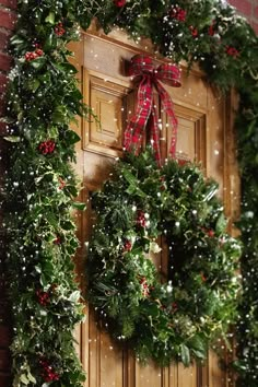 a christmas wreath hanging on the front door of a brick building with snow falling around it