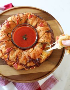 a person dipping sauce into a deep dish pizza on a wooden platter with red checkered table cloth