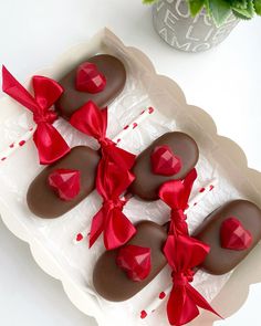 chocolate covered heart shaped candies in a box with red bows on them and a potted plant next to it