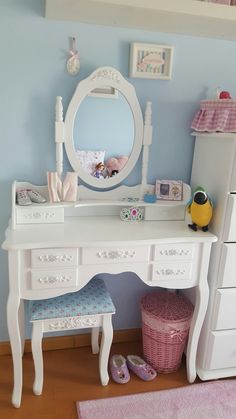 a white desk with a mirror, stool and toy chest in the corner next to it