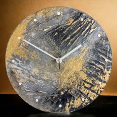 a clock made out of metal with gold and black paint on the face, sitting on a table