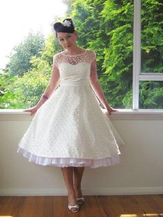 a woman standing in front of a window wearing a white dress with polka dots on it