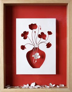 a red vase with flowers cut out of paper on a white background in a wooden frame