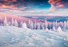 snow covered trees and mountains under a cloudy sky with clouds in the distance, at sunset