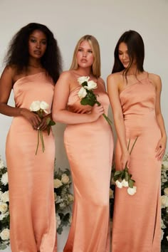 three beautiful women in long dresses standing next to each other with flowers on their bouquets