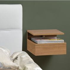 a nightstand with magazines on it next to a white chair and green wall behind it