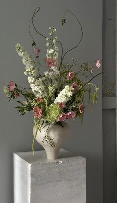 a white vase filled with lots of flowers on top of a block of concrete next to a window