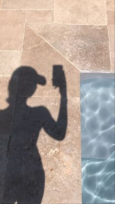 the shadow of a man holding a beer in his hand next to a swimming pool