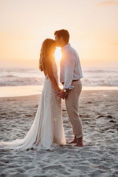 a bride and groom kissing on the beach at sunset