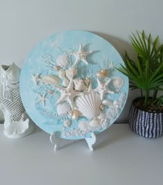 there is a blue plate with sea shells on it next to a potted plant