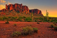 the sun is setting in the desert with mountains and cactuses behind it, as seen from across the valley