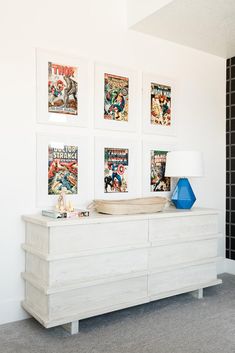 a white dresser sitting next to a wall with pictures on it and a blue lamp