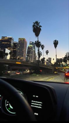 the view from inside a car looking at palm trees and city lights in the distance