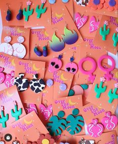 an assortment of earrings and brooches displayed on orange cards with pink envelopes