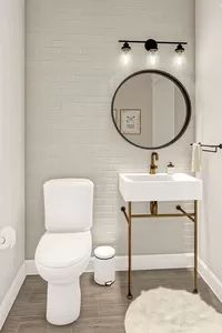 a white toilet sitting next to a sink in a bathroom under a large round mirror