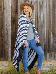 a woman standing in front of a wooden fence wearing a black and white striped blanket