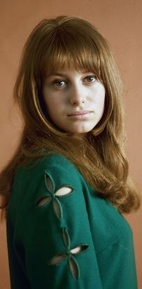 a woman with long red hair wearing a green dress and looking at the camera while standing in front of a brown wall