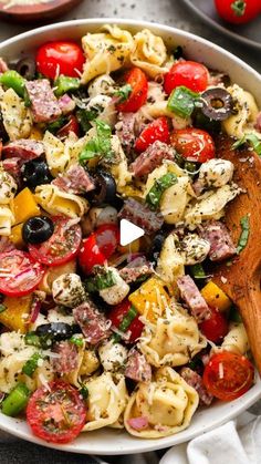 a pasta salad with tomatoes, olives, and other ingredients in a white bowl