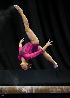 a woman on the balance beam doing a handstand in front of a black background