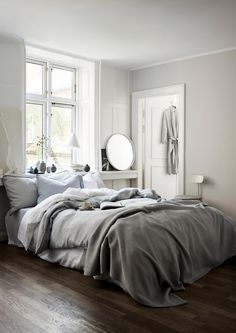 an unmade bed sitting next to a window in a room with wooden floors and white walls