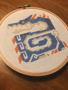 a cross stitch pattern on a wooden table with a needle in the shape of a car