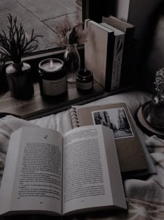 an open book sitting on top of a bed next to two candles and some books