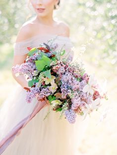 a woman holding a bouquet of flowers in her hand and wearing a dress with an off the shoulder neckline